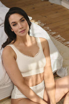 Woman wearing a white mastectomy bra and panties set sitting on a bed.